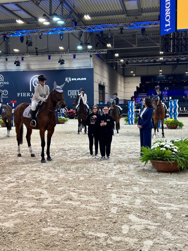 Due ragazze della squadra Ape'n Down in divisa nera al centro dell'arena di Fieracavalli, tra cavalli e cavalieri in gara