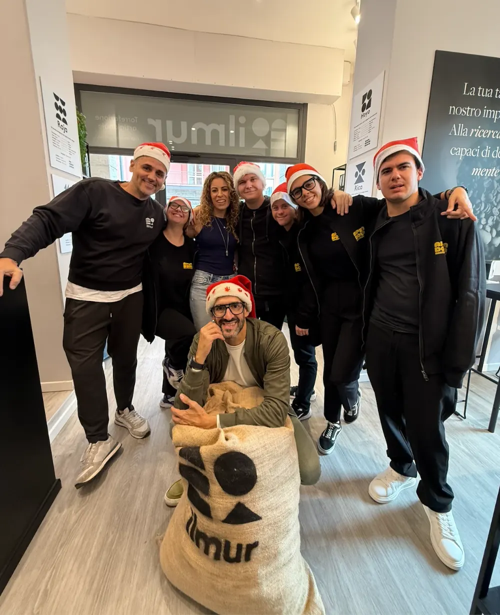 Il team di Ape'n Down con i cappelli di Babbo Natale nella torrefazione Ilmur, intorno a un sacco di caffè Ilmur