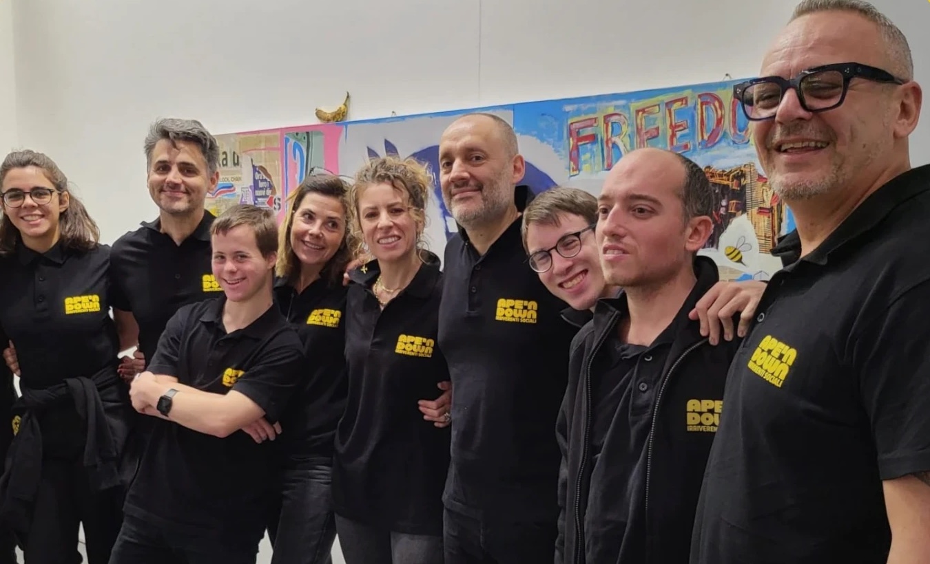Il team di Ape'n Down in polo nera con il logo giallo, in fila e sorridente davanti a un murale colorato